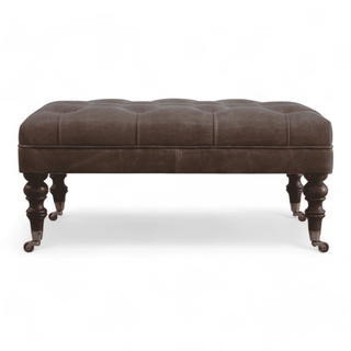 Front view of the brown tufted leather bench with ornate wooden legs.