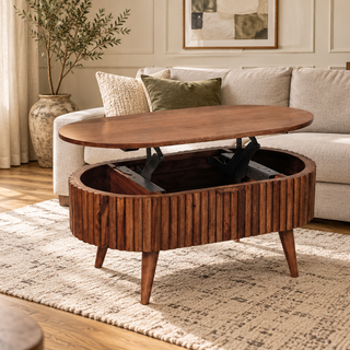 An oval wooden lift-top coffee table with a ribbed side and four tapered legs, shown in a bright living room with a sofa, rug, and plants.