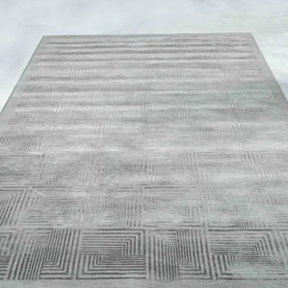 A square gray area rug with a textured geometric pattern of concentric lines and maze-like squares, shown from a high-angle perspective against a light gray background.