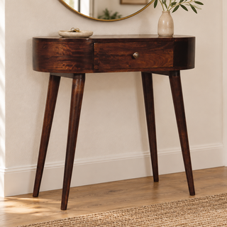 A dark brown wooden console table with a single drawer and tapered legs, styled in a bright, modern room with a mirror and vase on top.