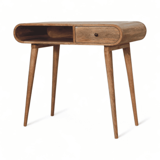 Angled view of a mid-century modern writing desk made from natural mango wood with curved edges, a single drawer, and open storage space.