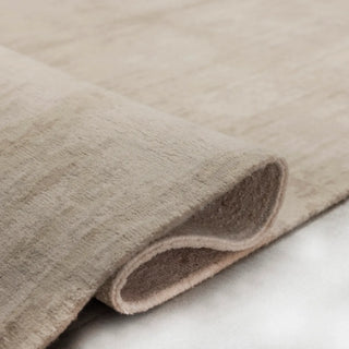 Edge of a beige wool rug curled back to show the hand-knotted reverse side