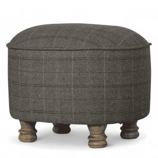 A round upholstered ottoman stool with a dark gray herringbone patterned fabric and four turned wooden legs, shown against a plain white background.