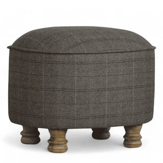 A round upholstered ottoman stool with a dark gray herringbone patterned fabric and four turned wooden legs, shown on a white background.