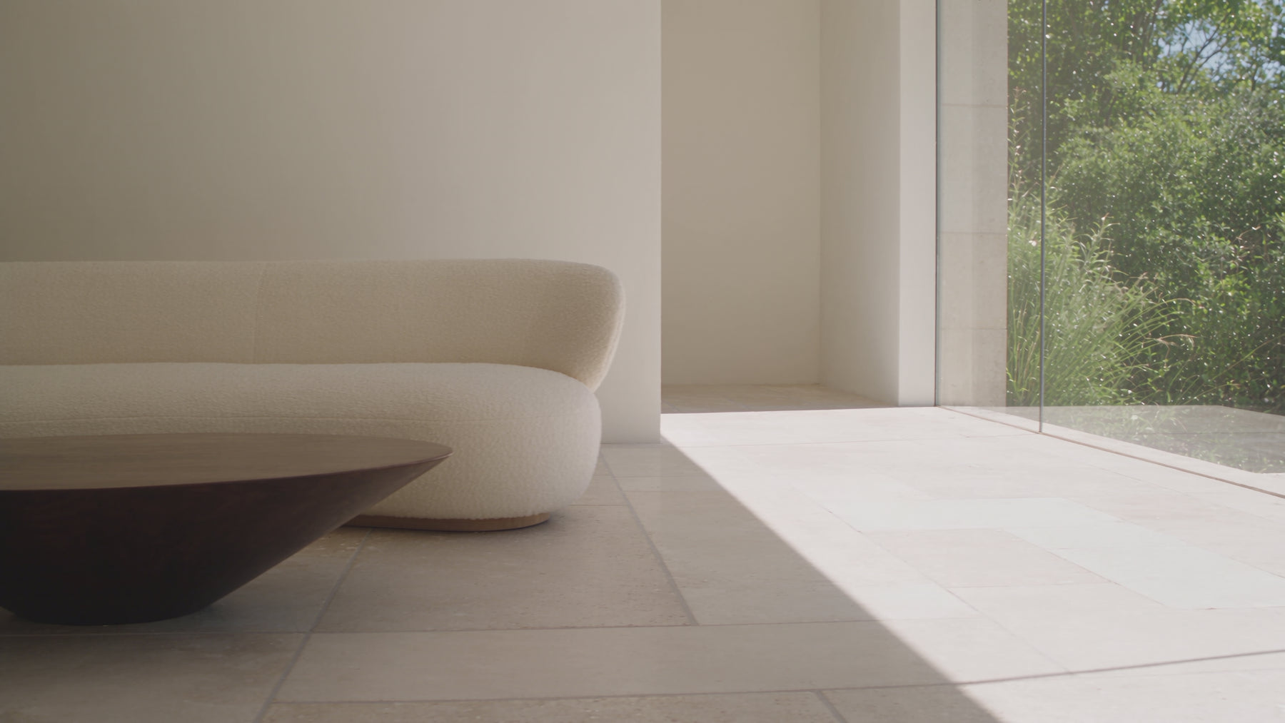 Cinematic video of a cream curved sofa and sculptural dark wood coffee table in a sunlit room, followed by a close-up of a hand touching a warm wood surface.